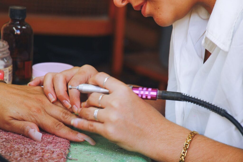The Art of Drawing Readers In: Your attractive post title goes here Close-up image of a nail technician using an electric file on a client's nails during a manicure session.